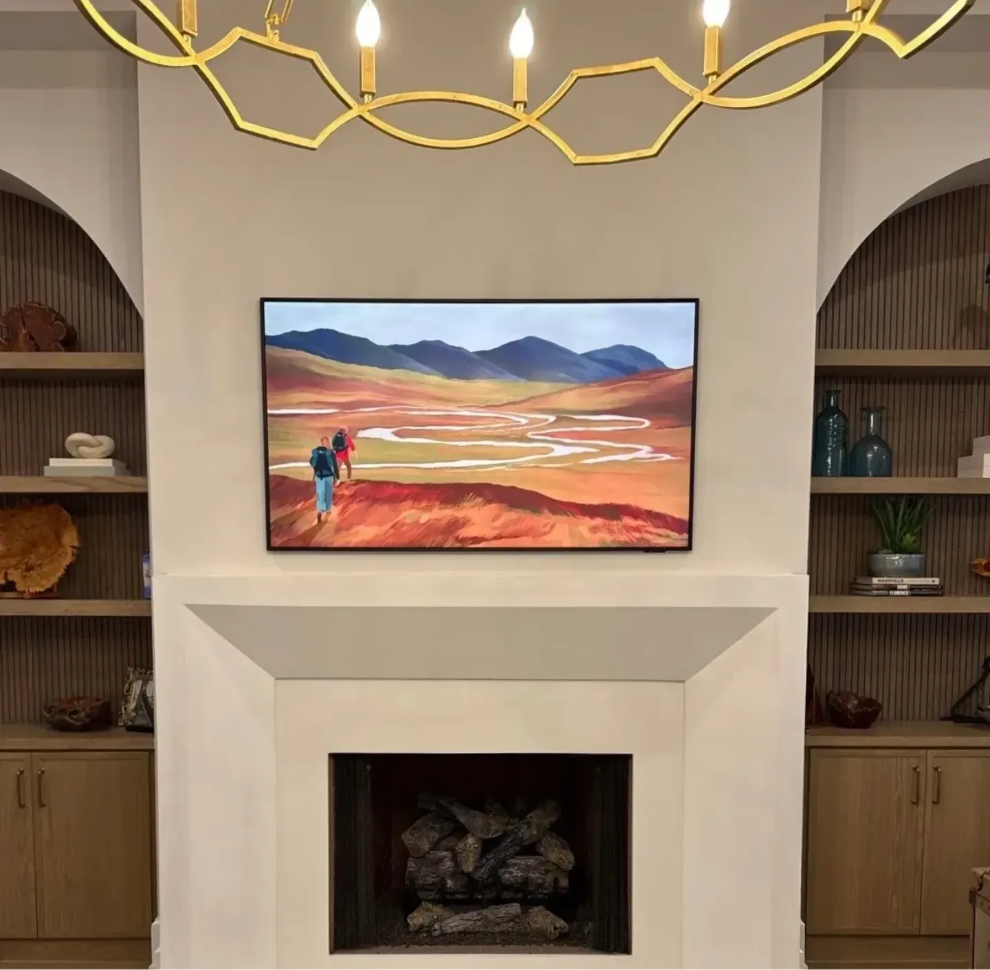 Framed TV showing a landscape over a plaster fireplace, arched built-ins and a gold chandelier