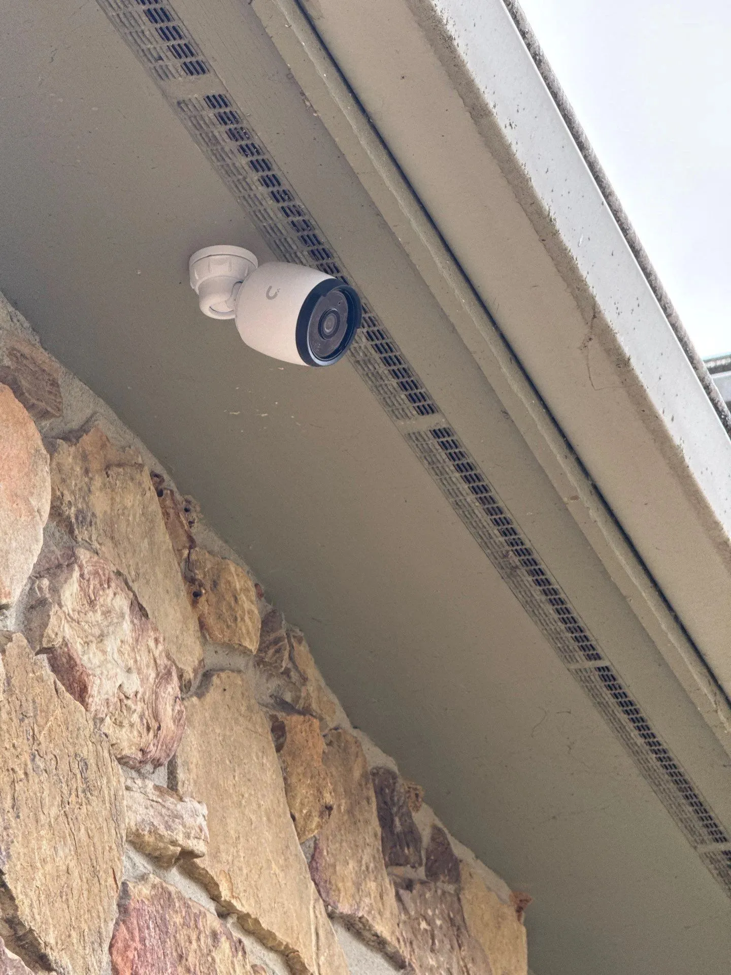 Security camera mounted under an eave beside a stone chimney