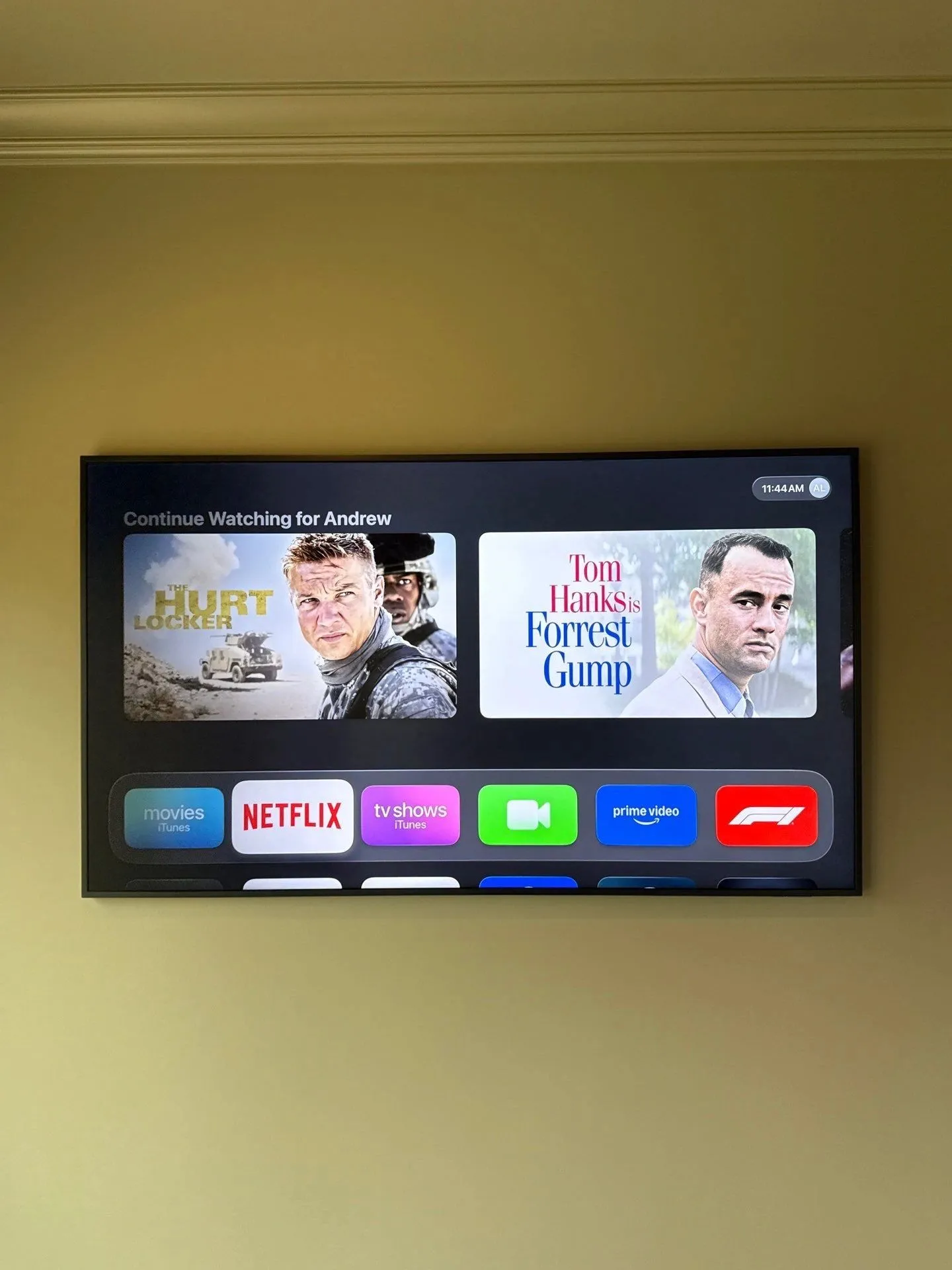 Wall-mounted TV on a gold wall showing the Apple TV home screen