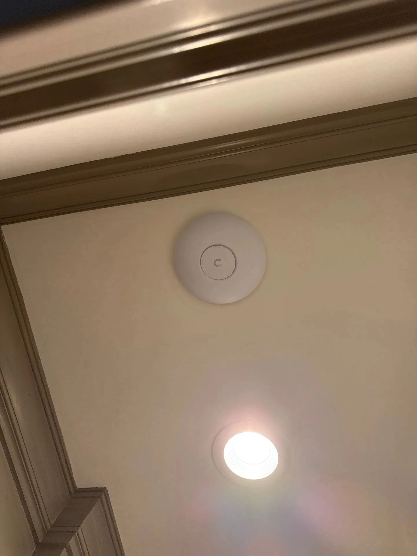 Wi-Fi access point mounted flush in a tray ceiling beside a recessed light